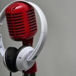 Close-up of a red vintage microphone with white headphones against a gray background.