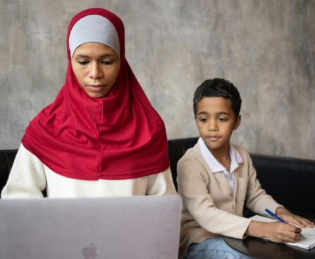 Muslim pensive ethnic mother typing on netbook while son with pen taking notes in notebook