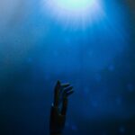 Silhouette of a robotic hand reaching towards glowing blue light in a futuristic setting.