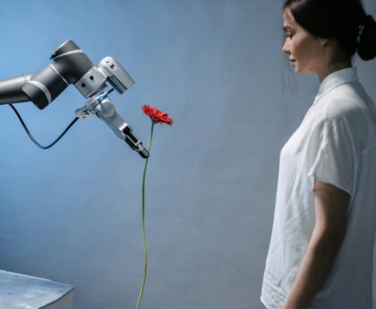 A woman observes a robot holding a red flower, symbolizing technology and nature integration.