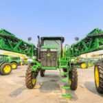 A green agricultural tractor with extended arms displayed outdoors under a blue sky in Burley.