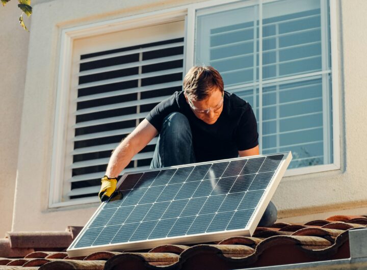 A worker installing a solar panel on a residential rooftop under bright sunlight.
