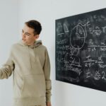 Enthusiastic teen boy in a hoodie teaching math on a blackboard.