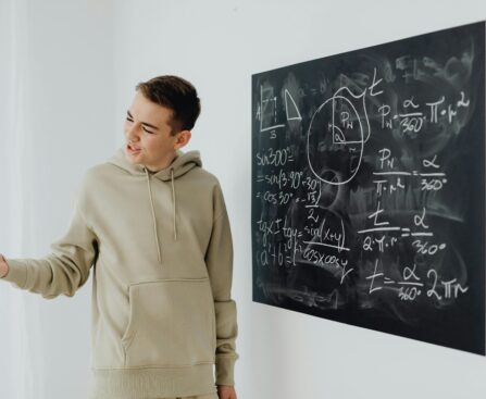 Enthusiastic teen boy in a hoodie teaching math on a blackboard.