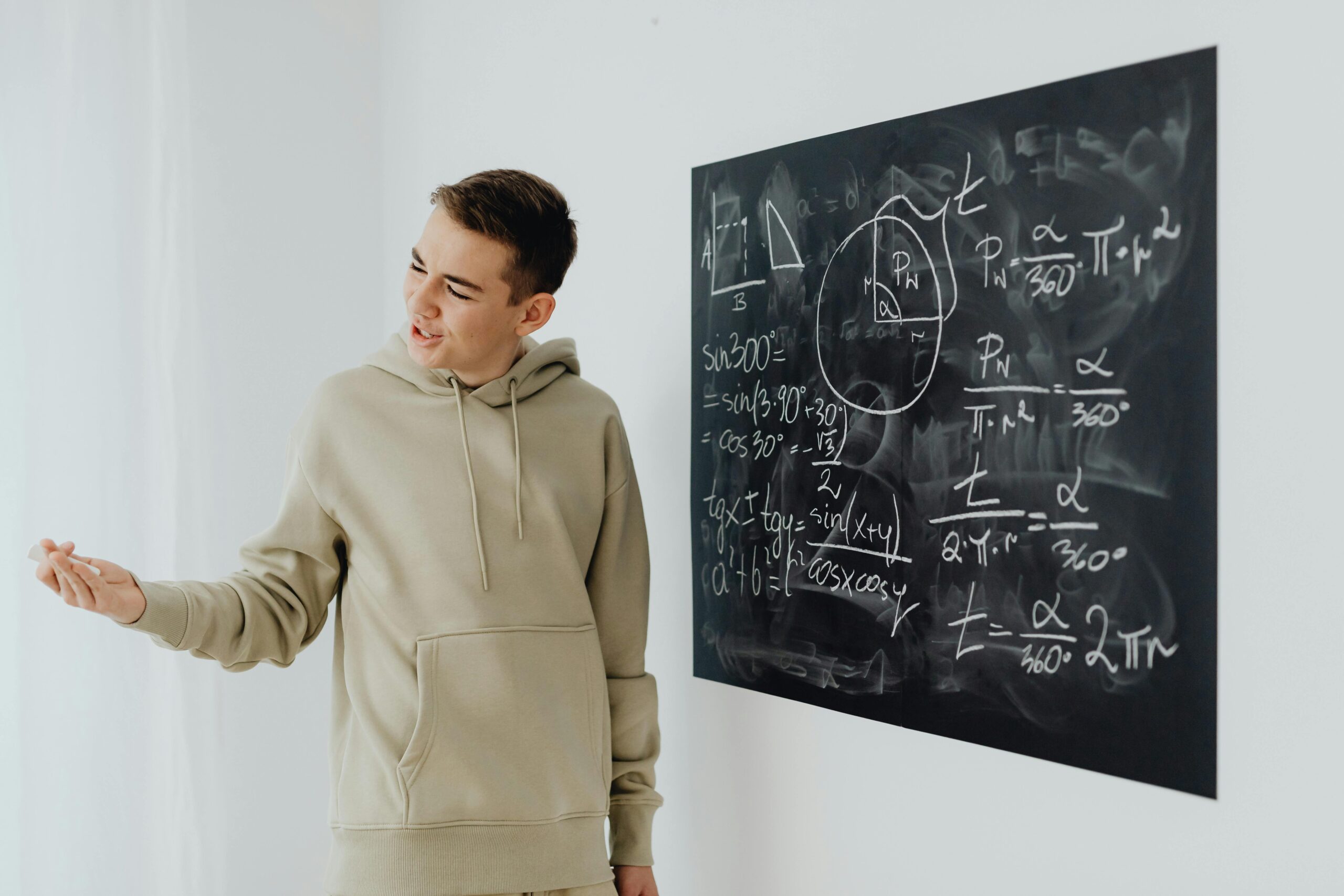 Enthusiastic teen boy in a hoodie teaching math on a blackboard.
