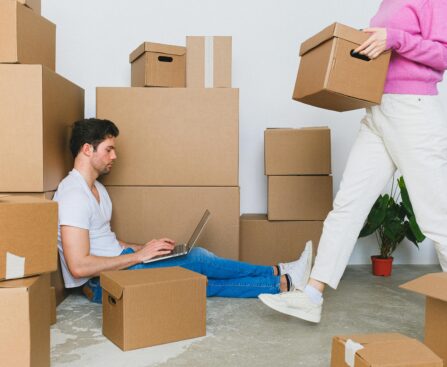 Young couple settling in new apartment surrounded by packing boxes, managing tasks on a laptop.