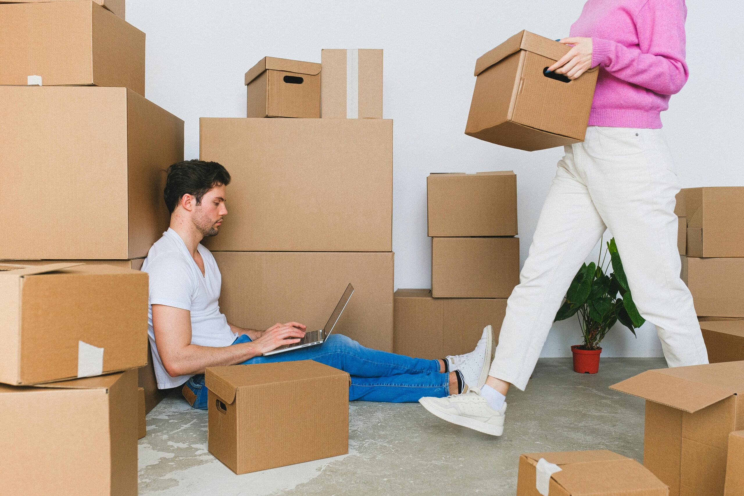 Young couple settling in new apartment surrounded by packing boxes, managing tasks on a laptop.