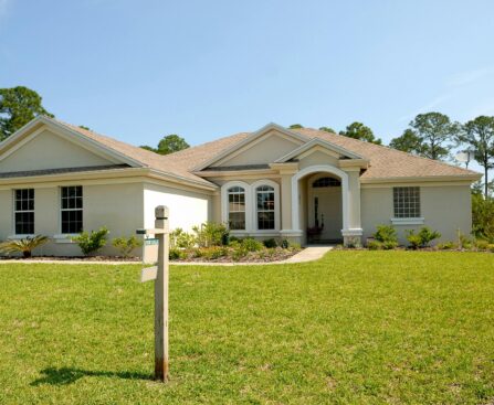 Beautiful suburban house with lush lawn, showcasing a for sale sign under a clear blue sky.