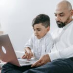 A father and son spending quality time together using a laptop, bonding in a cozy indoor setting.