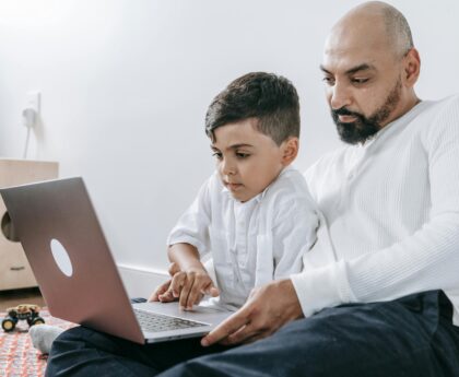 A father and son spending quality time together using a laptop, bonding in a cozy indoor setting.